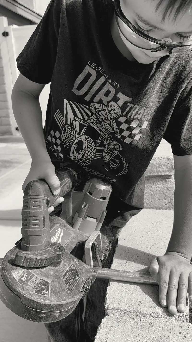 A young participant in safety glasses cutting conduit with a band saw