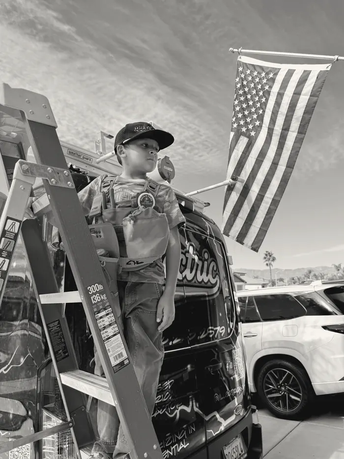 A young participant in a tool vest on a ladder beside the illectric van